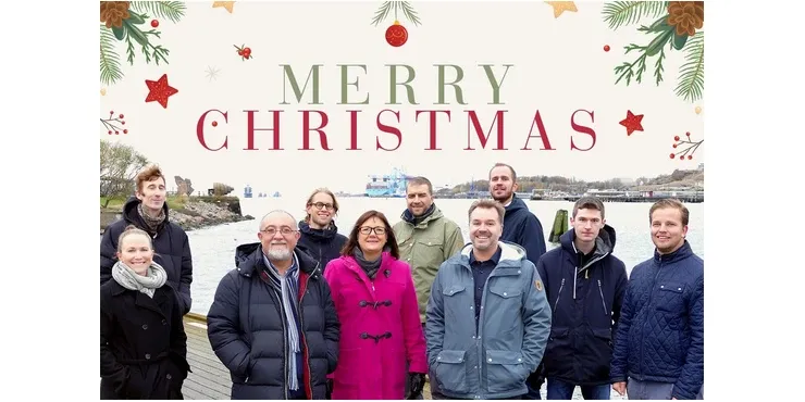 A Christmas card with the text “Merry Christmas” in spruce sprigs and baubles, and a photograph of SeaTwirl’s employees in winter clothes by the water