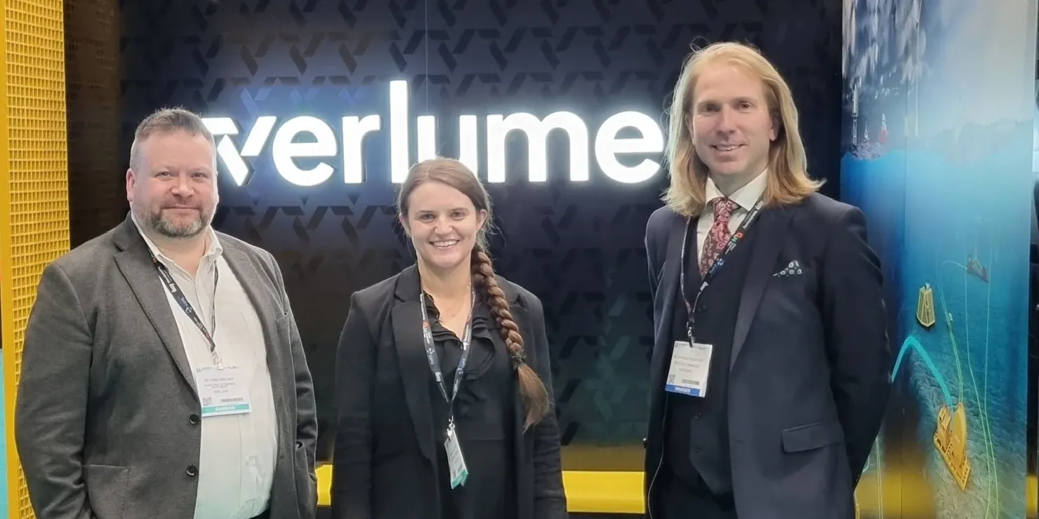 Three people in front of Verlume’s illuminated exhibition stand at Subsea Expo