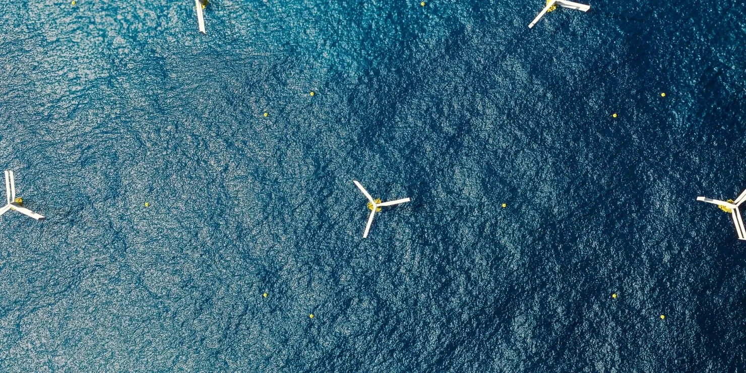 Six floating vertical-axis wind turbines seen from directly above, spread across a dark blue sea
