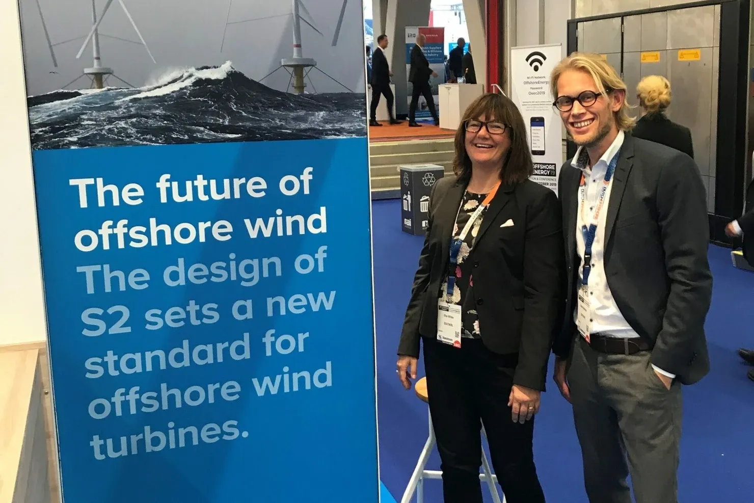 Two people at SeaTwirl’s blue exhibition wall with the text “The future of offshore wind”, in an exhibition hall