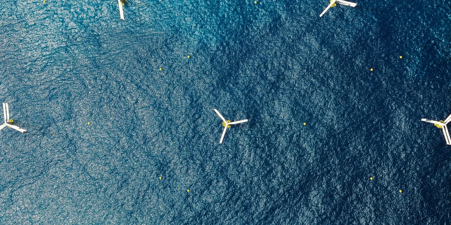 Six floating vertical-axis wind turbines seen from directly above, spread across a dark blue sea