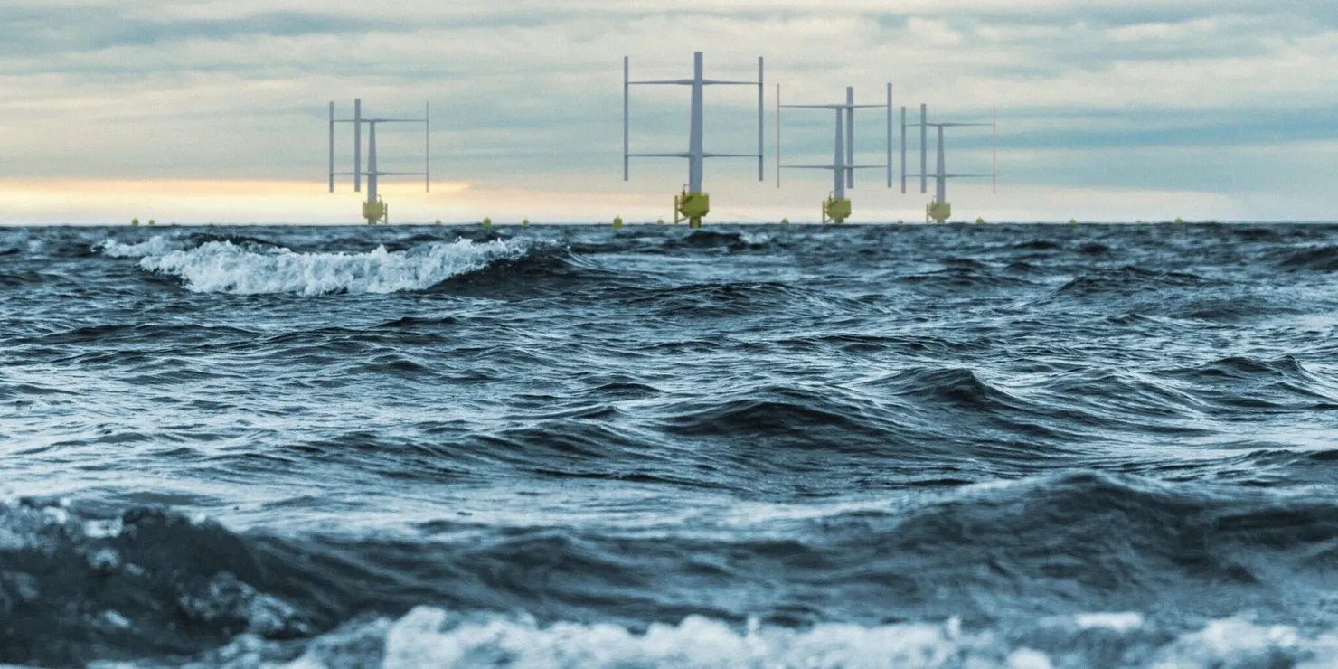 A row of vertical-axis wind turbines on the horizon, seen low from the surface of the water with waves in the foreground