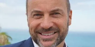 Peter Laurits leende i blå kavaj med havet bakom sig