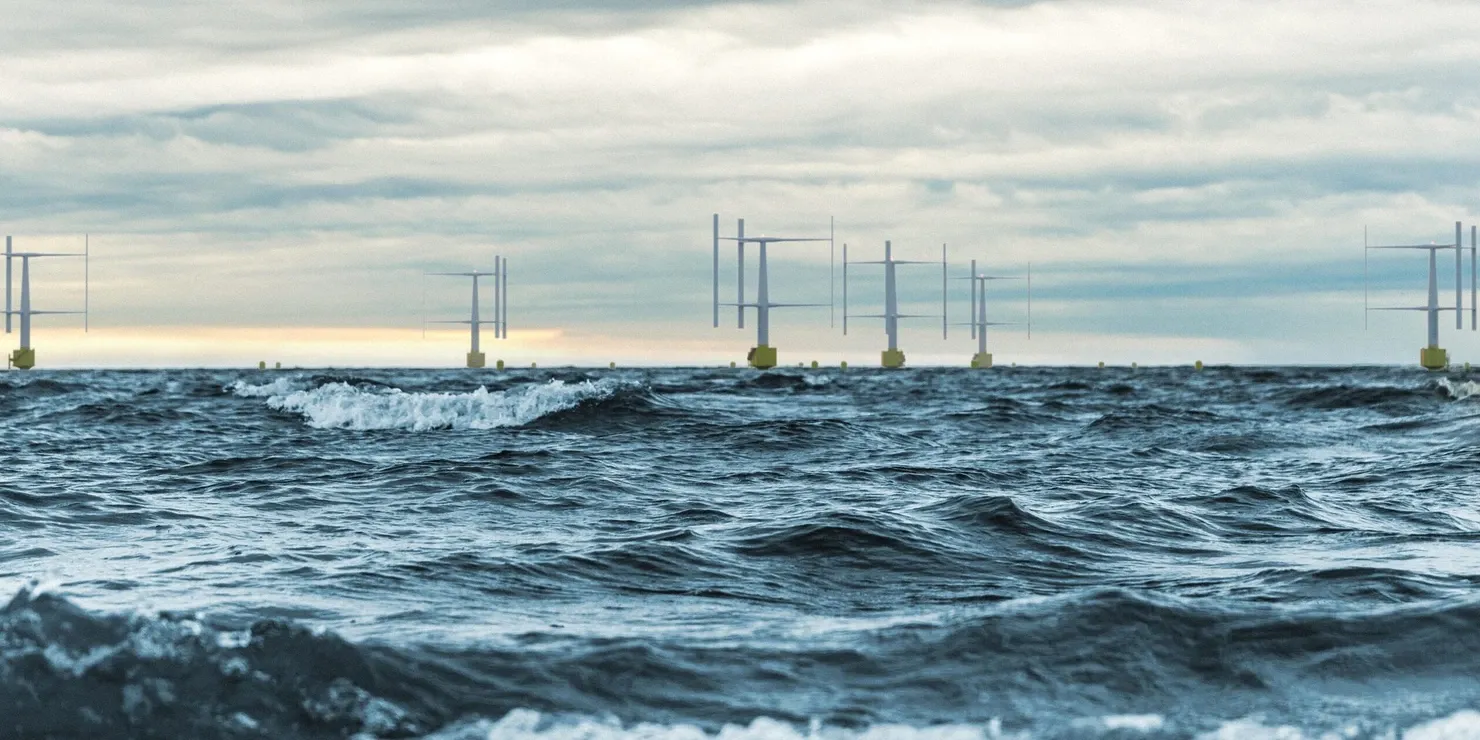 Vertical-axis wind turbines on the horizon in evening light, with waves in the foreground