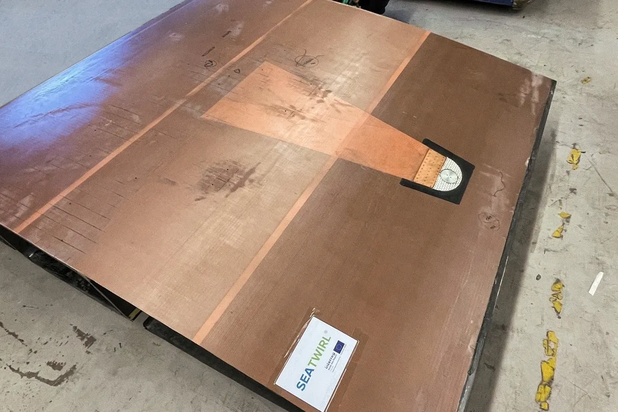 The brown mould for the blade section lying on a workshop floor with a person at the far end and a forklift truck behind