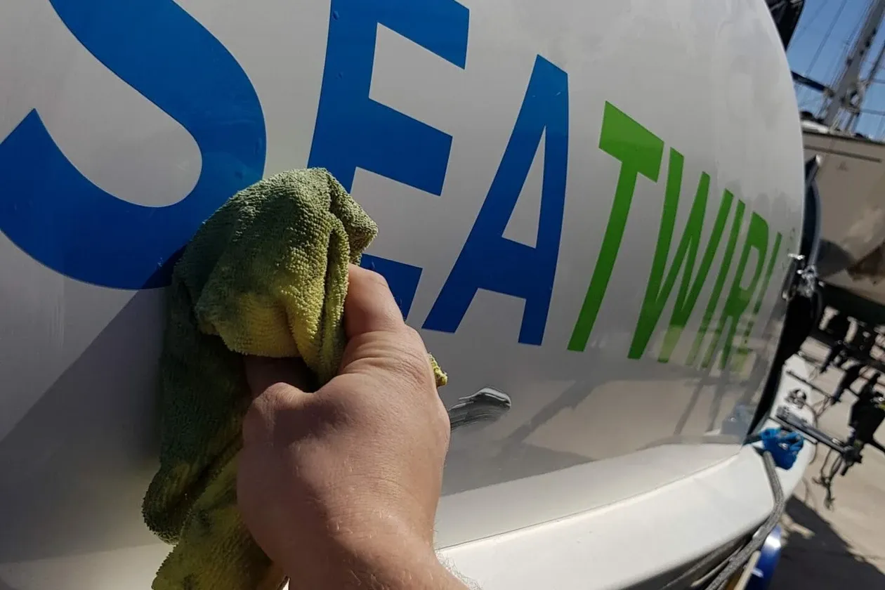 A hand polishing the hull of a white rowing boat carrying SeaTwirl’s logo